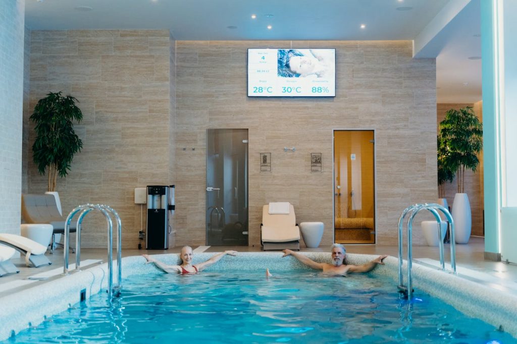 Two adults enjoying leisure time at an indoor swimming pool with spa-like ambiance.